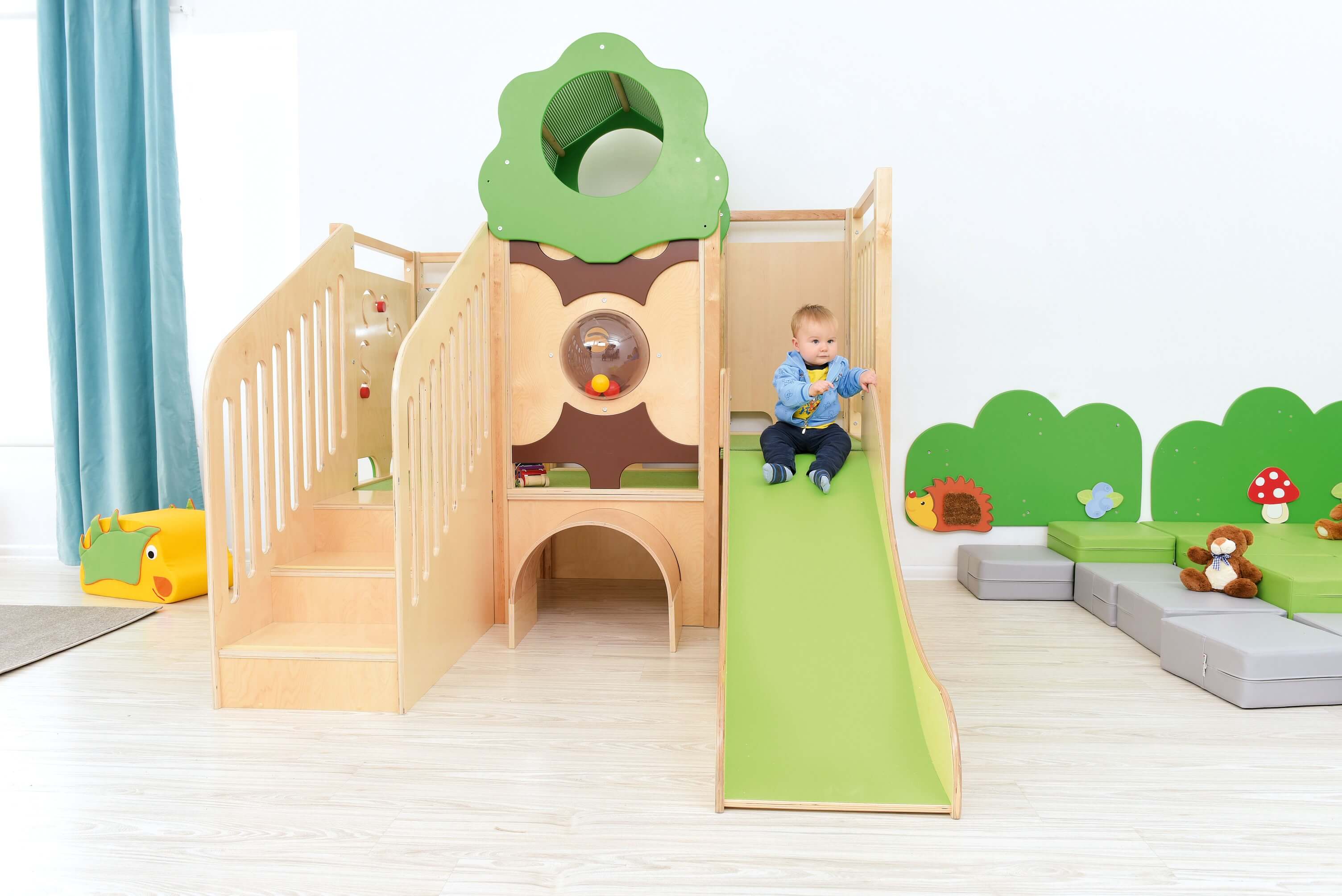 Kindergarten Spielpodest Vogelnest im Gruppenraum von vorne mit Kind auf Rutsche