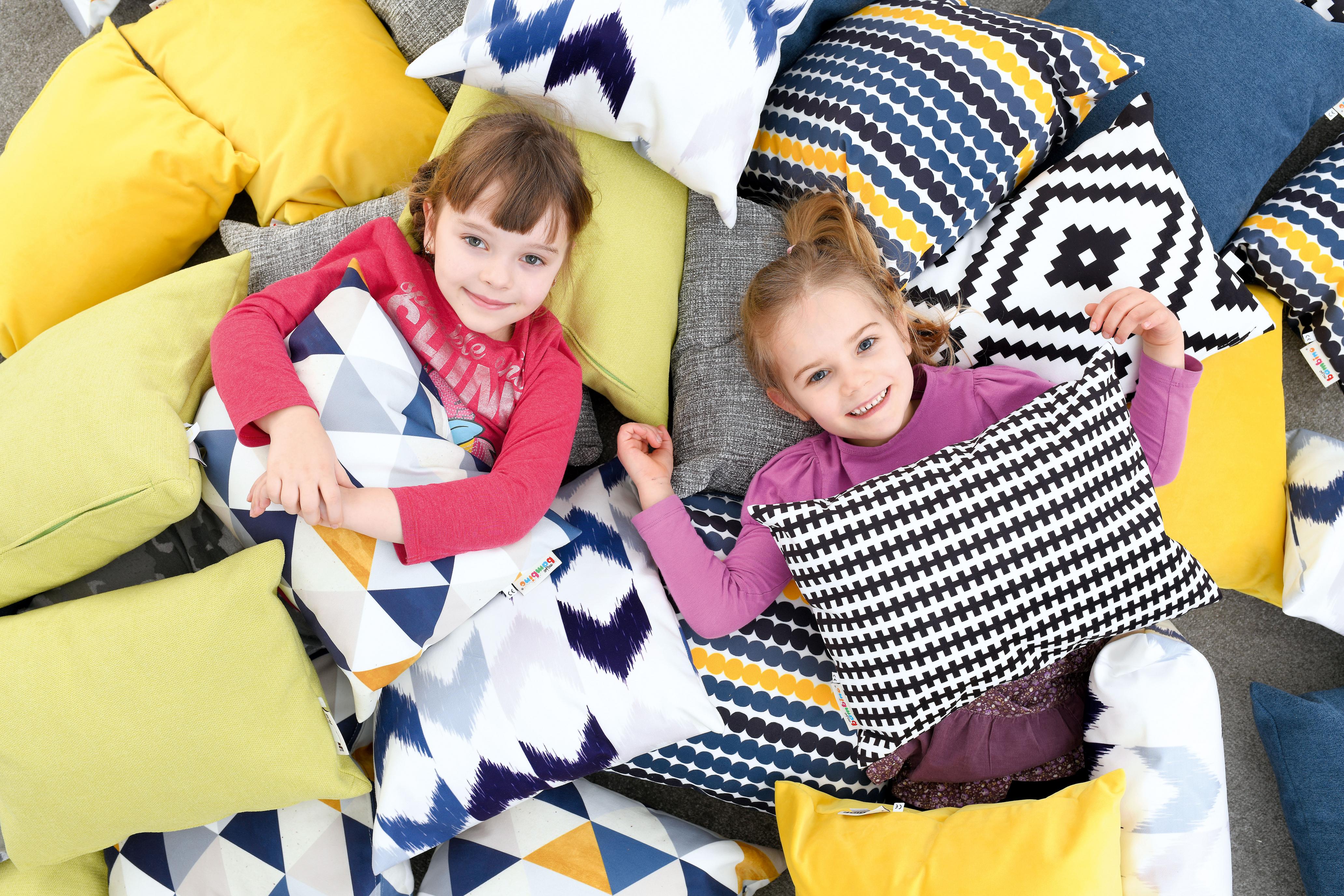Zwei Kinder liegen auf bunten Kissen für Sitzlandschaft.