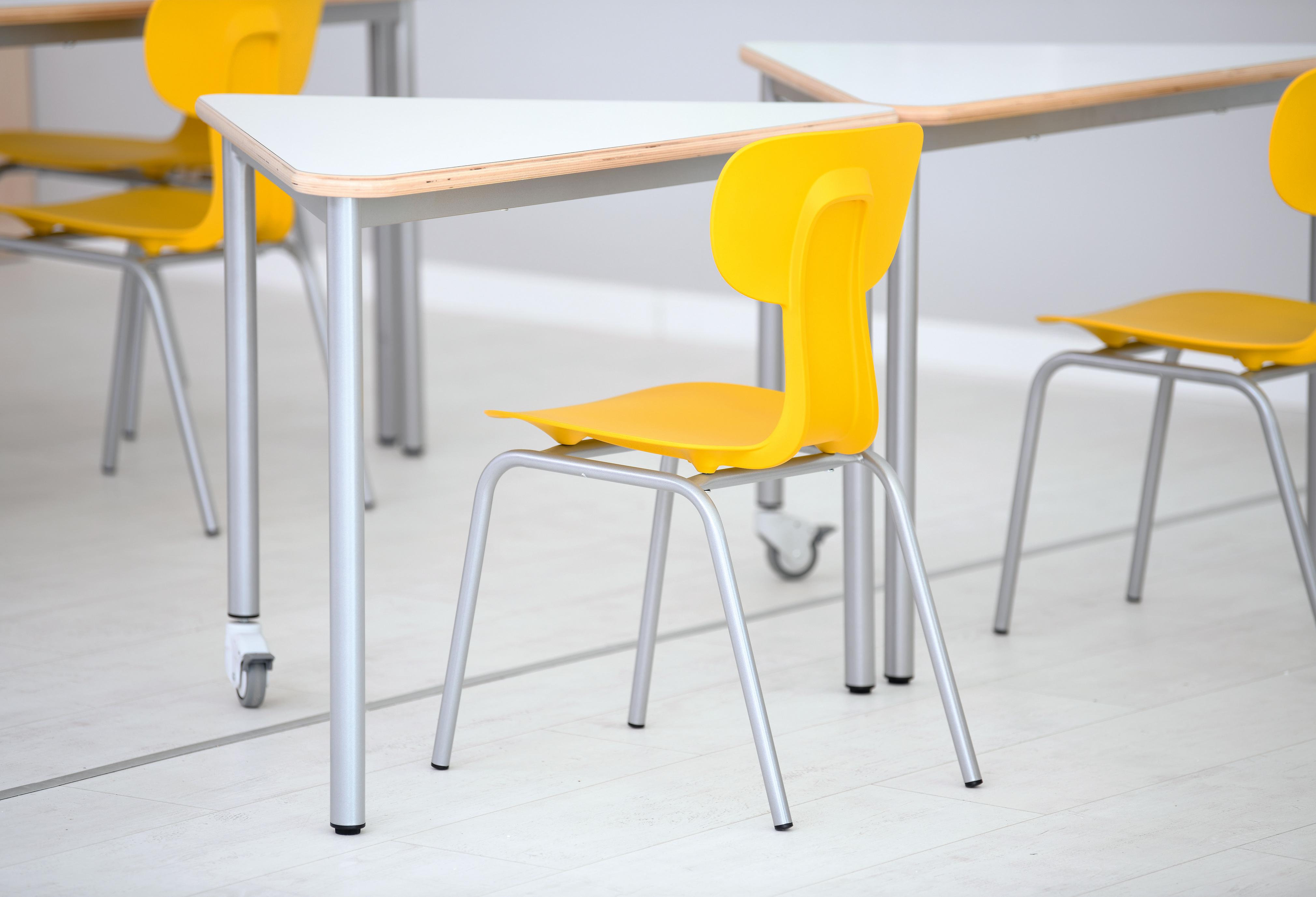 Gelber Schülerstuhl Ergo neben einem Tisch im Klassenzimmer.