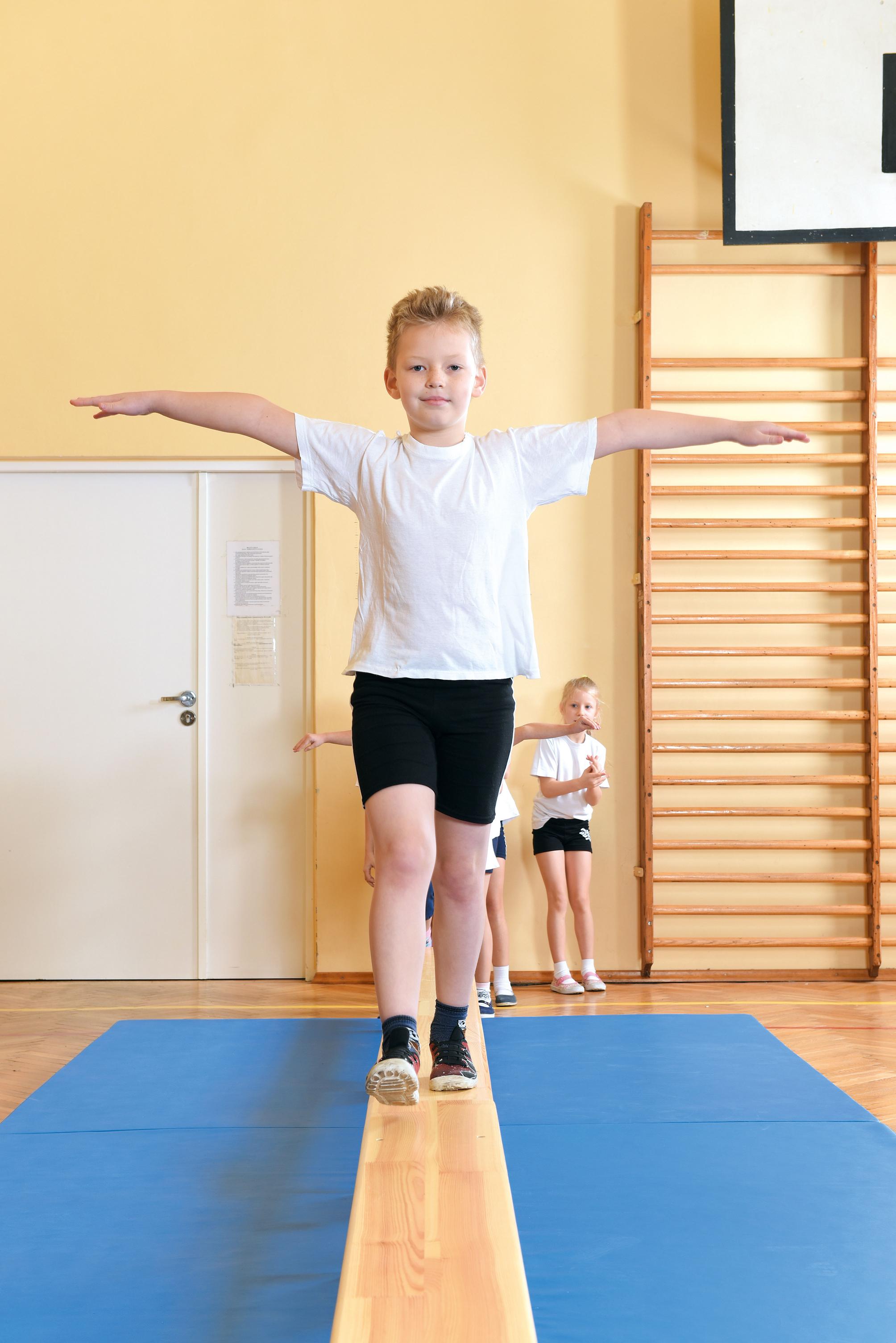 Kind balanciert auf der Turnbank 3 m im Raum.