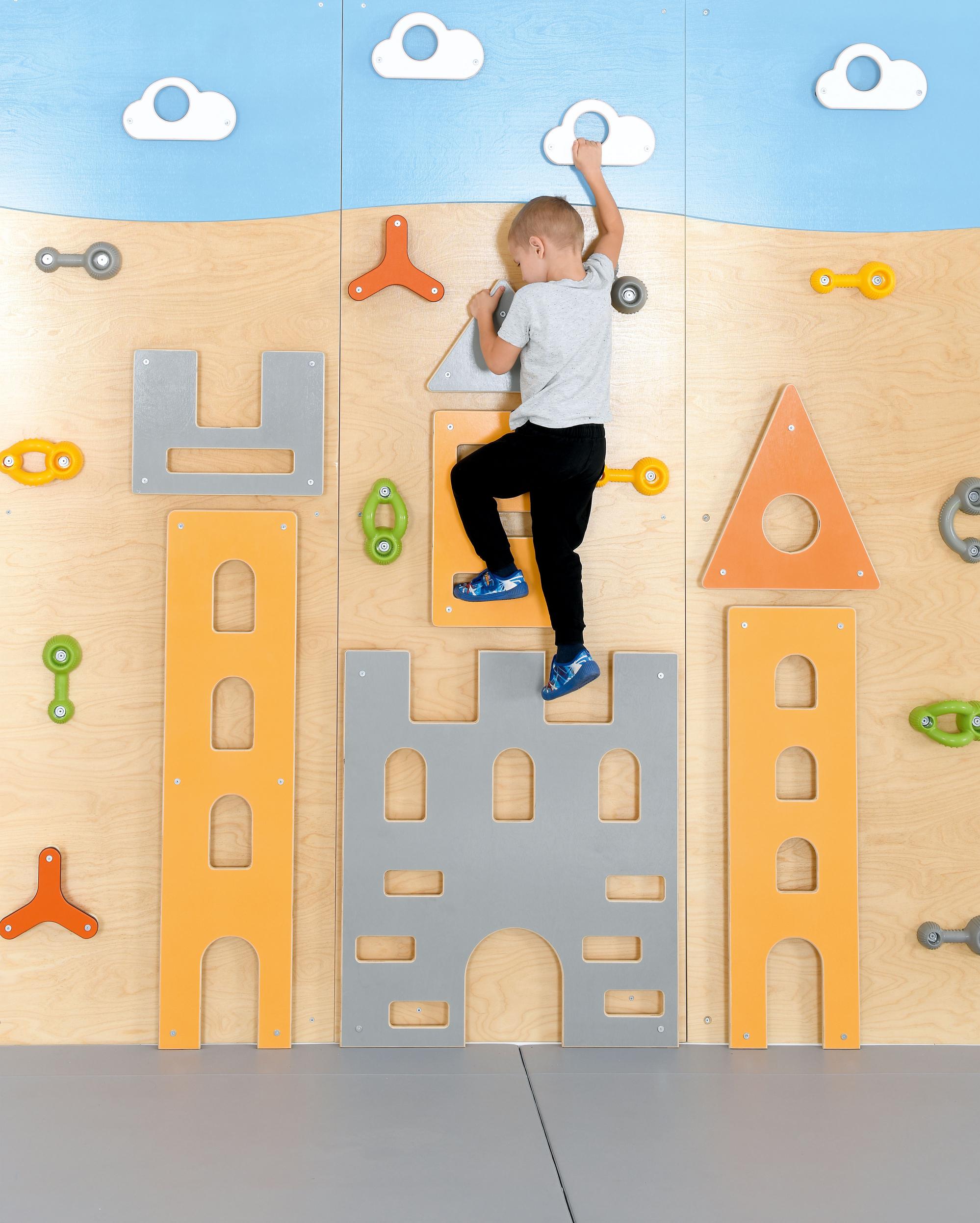 Kind klettert auf bunter Kletterwand im Gruppenraum.