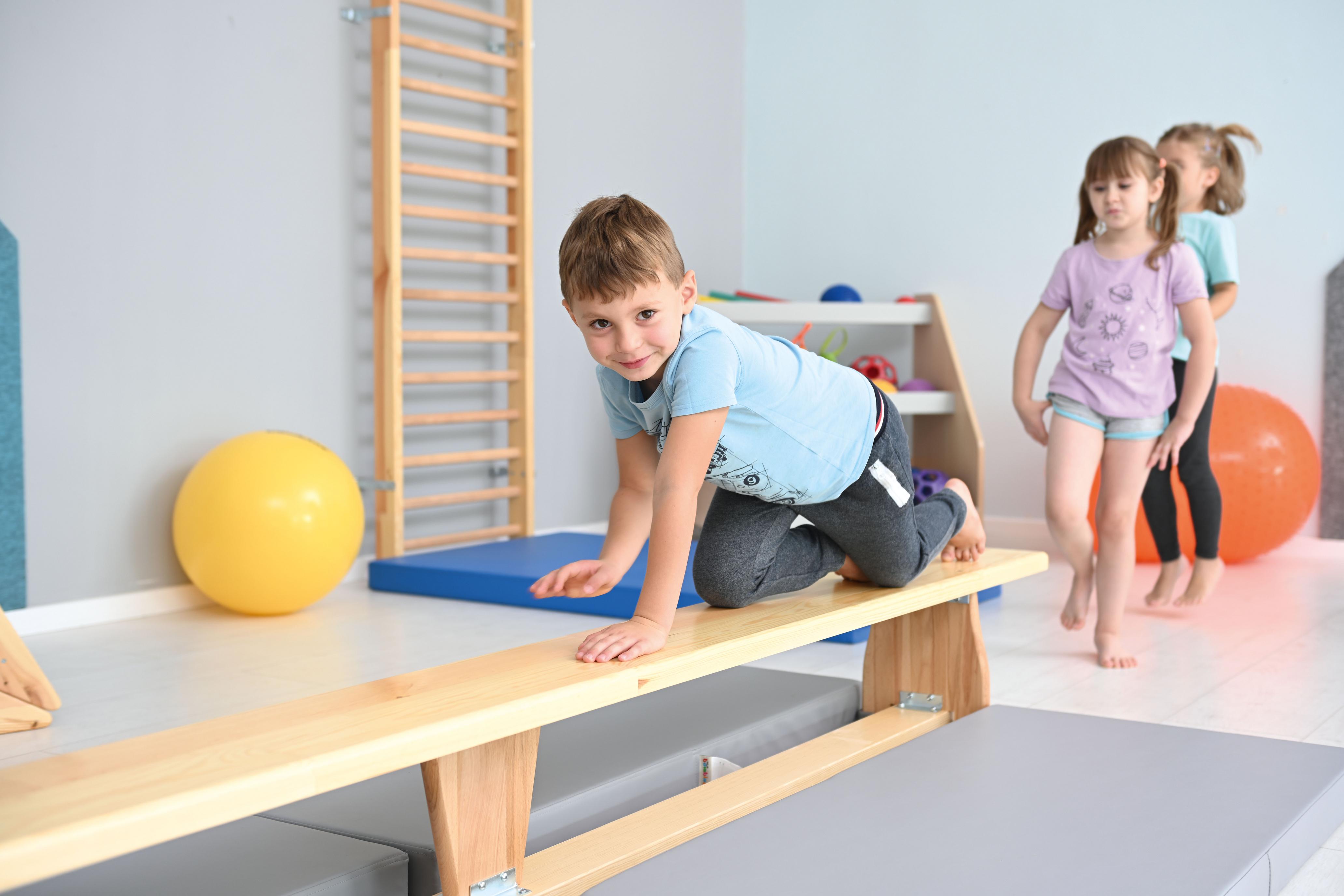 Kinder spielen auf Turnbank 3 m im Gruppenraum.