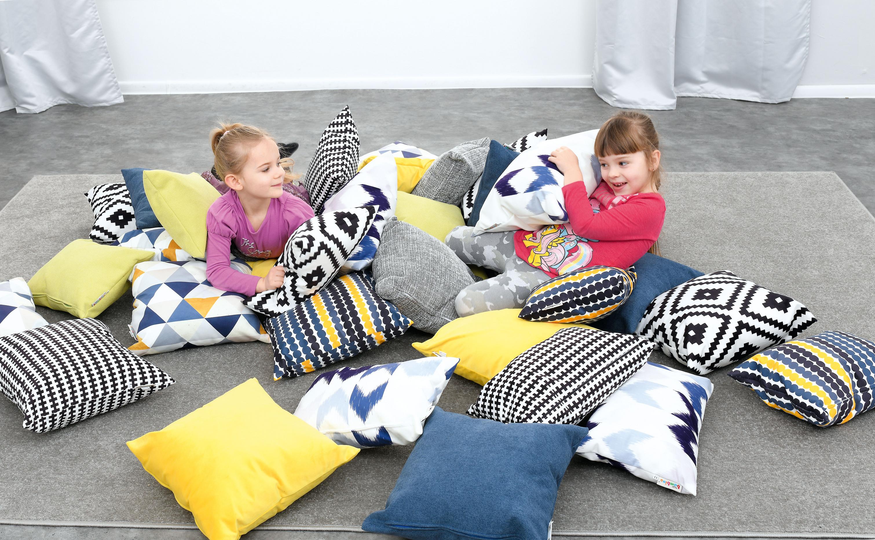 Kinder spielen mit Kissen für Sitzlandschaft im Raum.